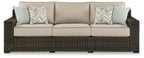Brown wicker sofa with three beige cushions and two patterned accent pillows