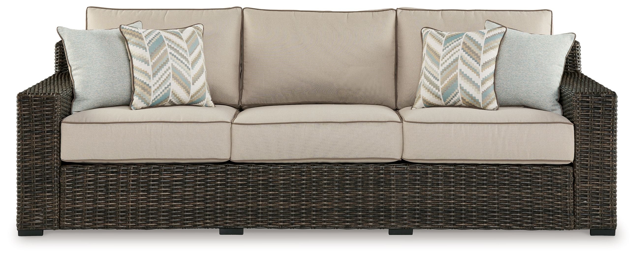 Brown wicker sofa with three beige cushions and two patterned accent pillows
