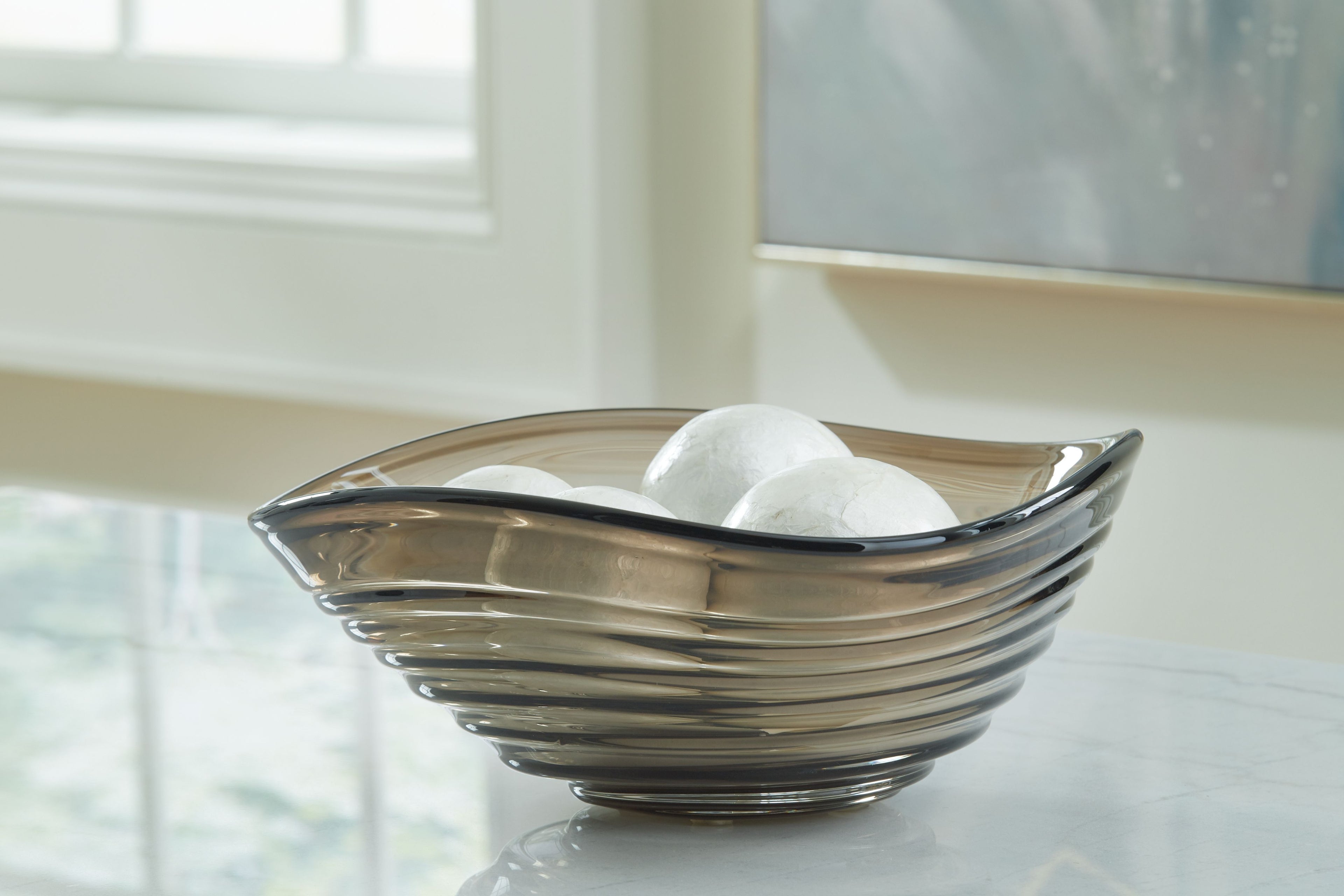 Solariston gray-brown glass bowl holding white decorative spheres, black rim