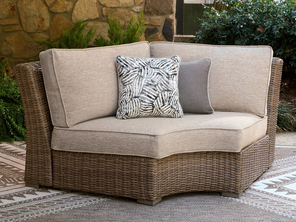Curved corner chair with beige seat cushion, woven wicker frame, and black-and-white pillow