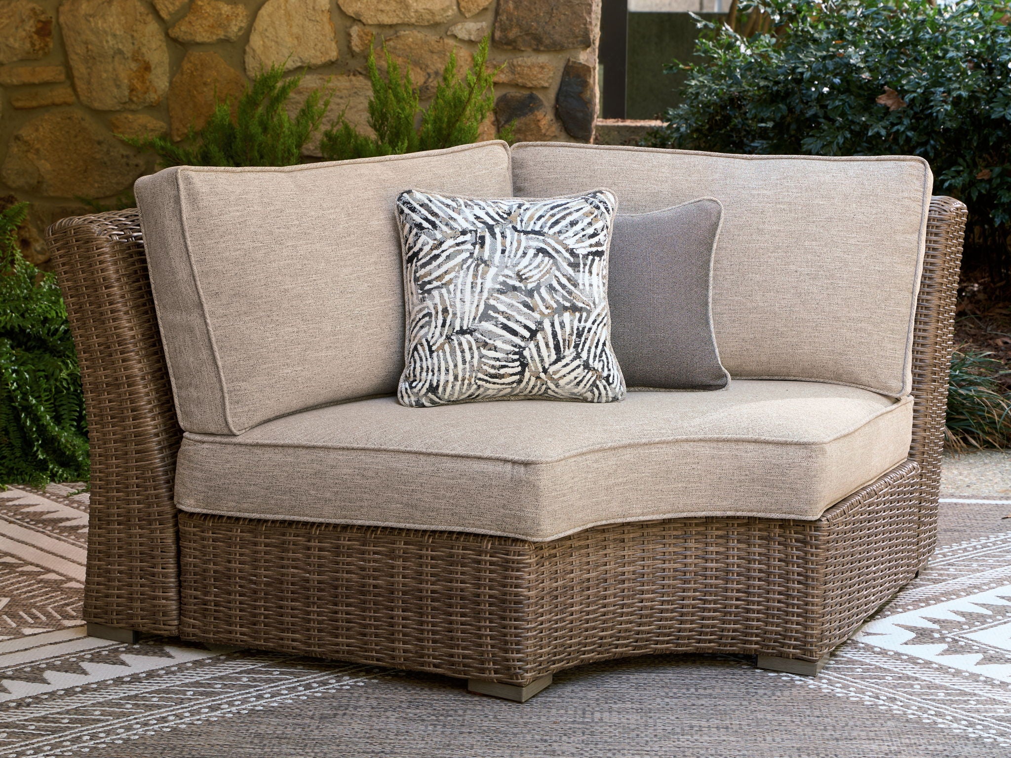 Curved corner chair with beige seat cushion, woven wicker frame, and black-and-white pillow