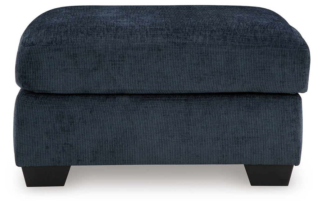 Dark navy upholstered ottoman with rounded square lid and dark block legs.