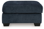 Dark navy upholstered ottoman with rounded square lid and dark block legs.