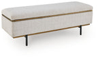 Stone upholstered storage bench with gold trim and dark tapered legs, hinged lid