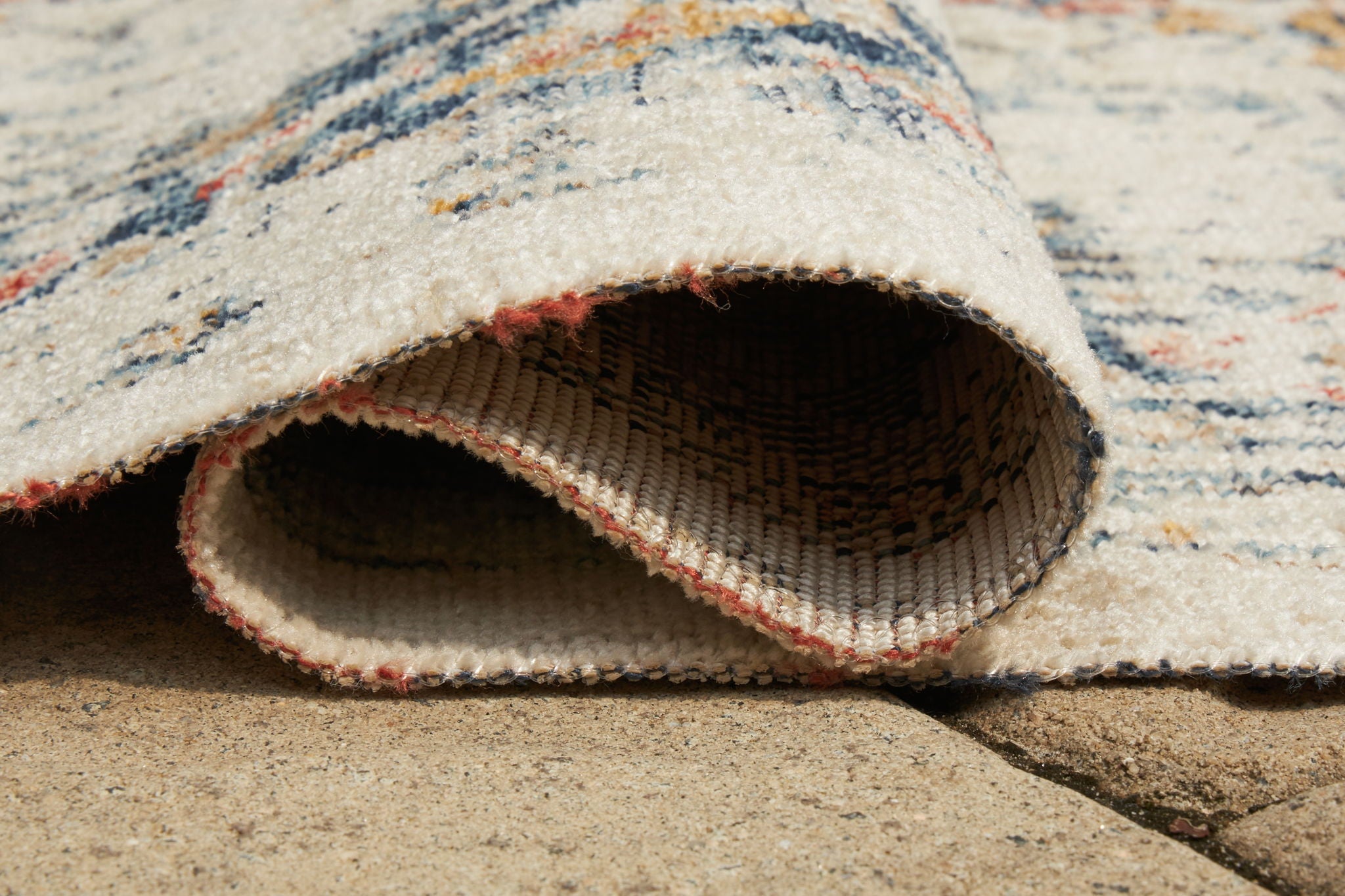 Multi-pattern area rug close-up of rolled edge; cream pile with blue and orange border