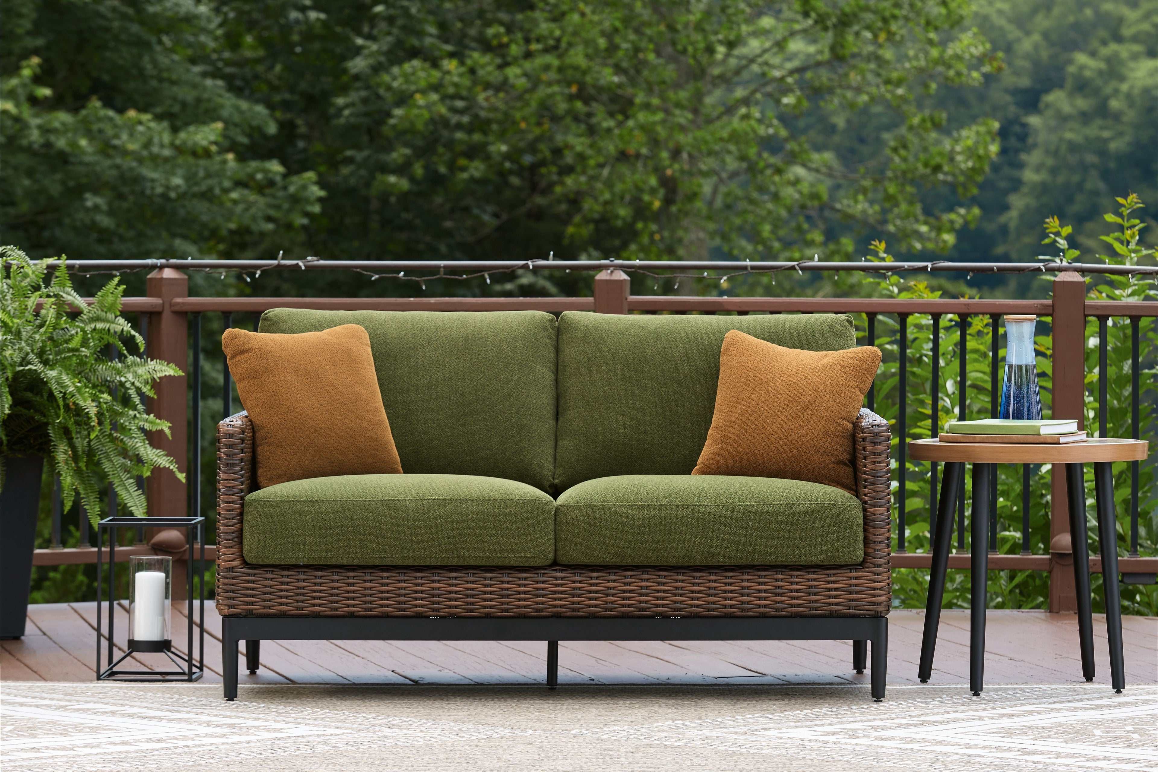 Outdoor loveseat with green cushions, brown woven wicker frame, and two brown accent pillows