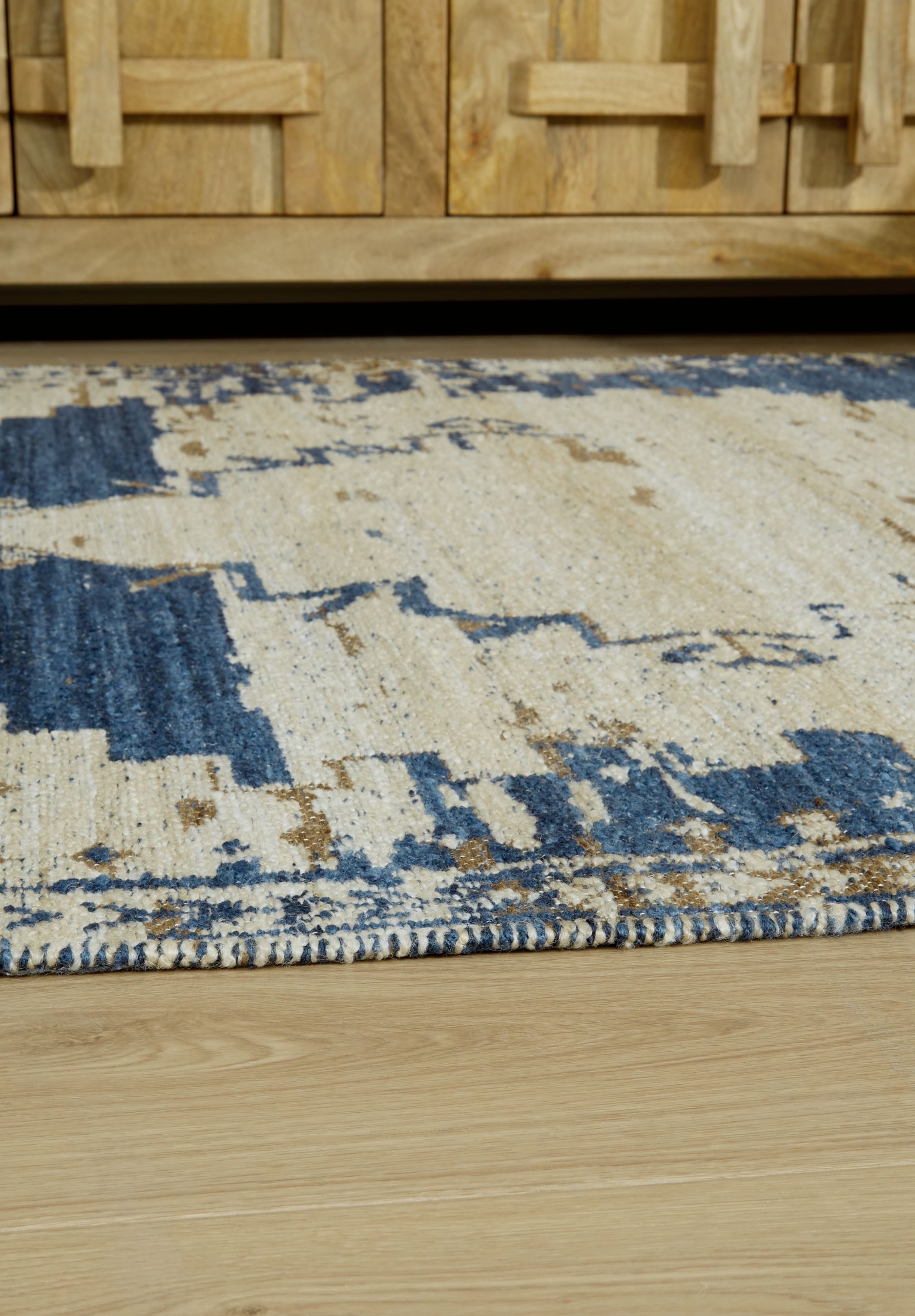 Corner view of cream, blue and tan geometric rug with distressed pattern