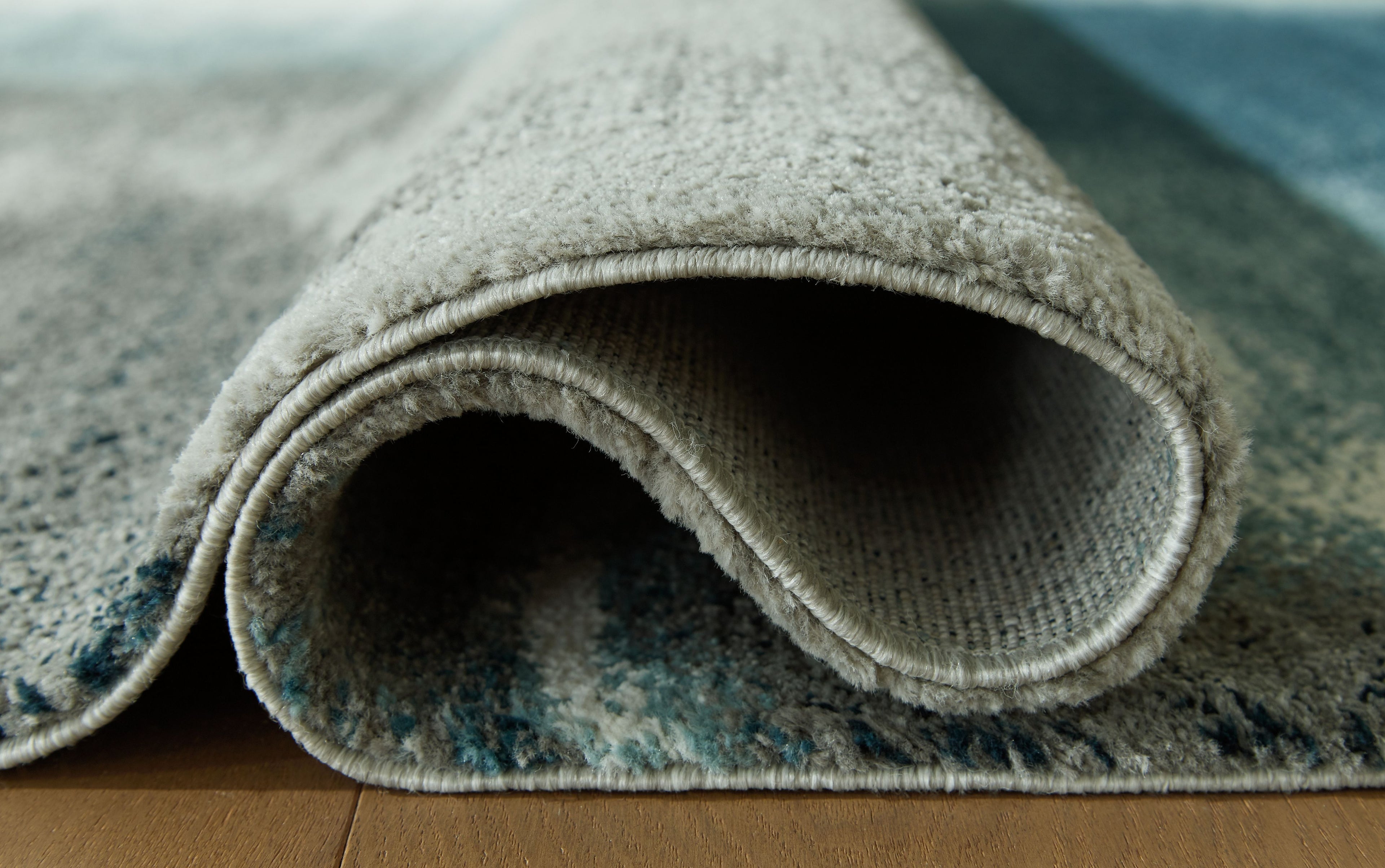 Blue area rug rolled edge showing short pile and stitched border, underside