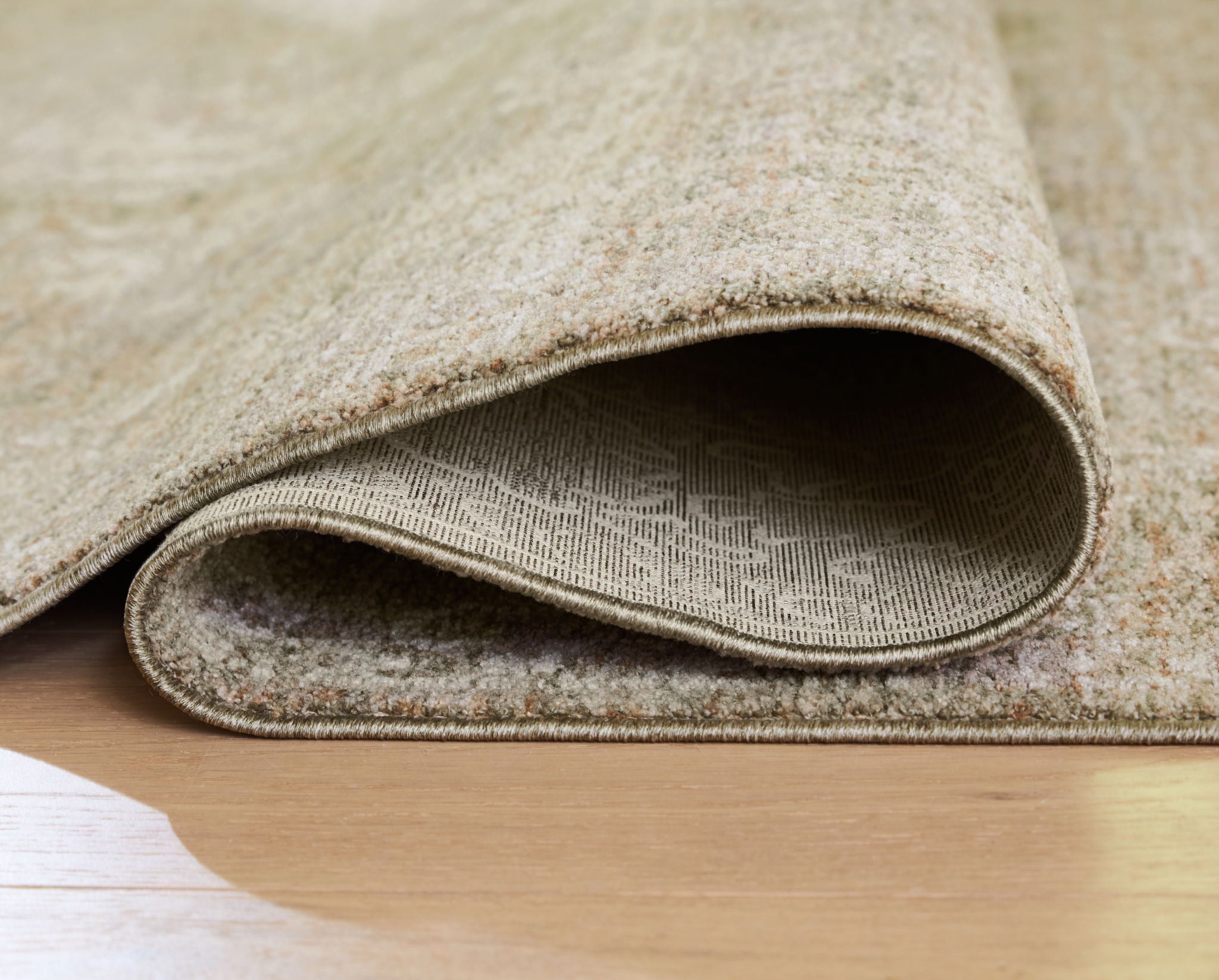 Light brown rug edge with low pile and stitched border, folded to show underside