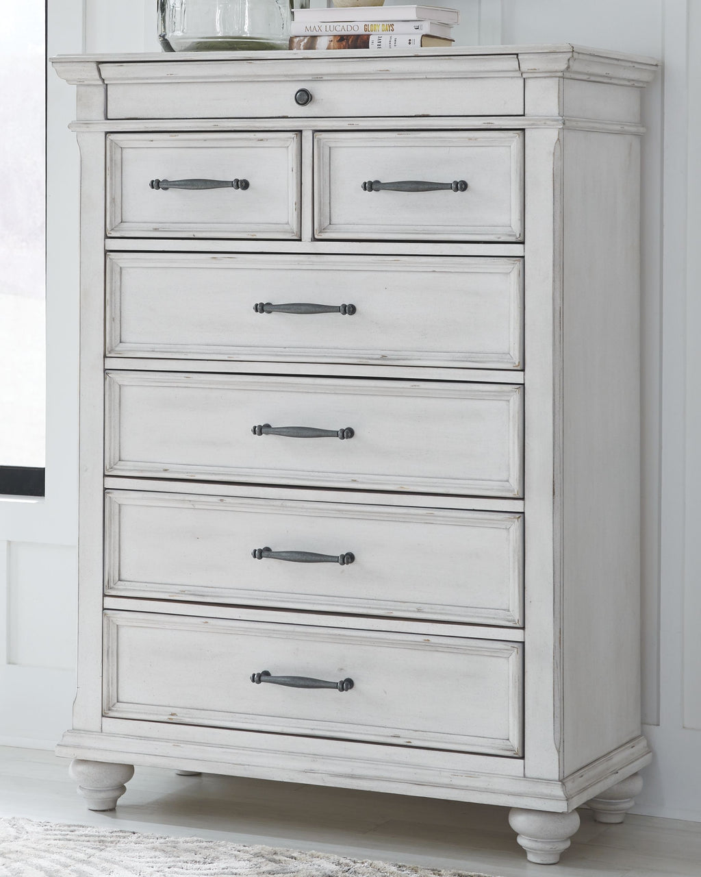White chest of drawers with six drawers and dark metal bar pulls, carved trim.