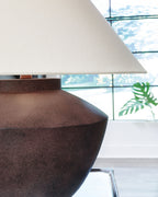 Antique brown table lamp from side, beige shade over textured round base