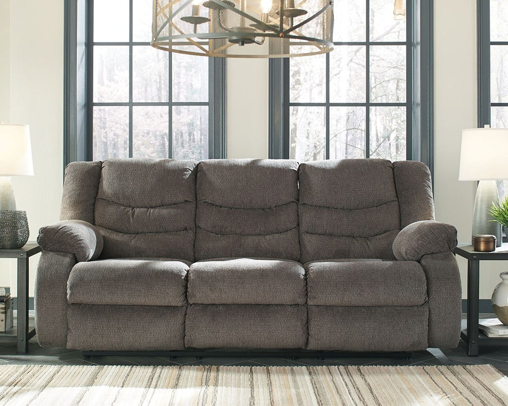 Gray reclining sofa with three seat sections, tufted back cushions, and recliner arms