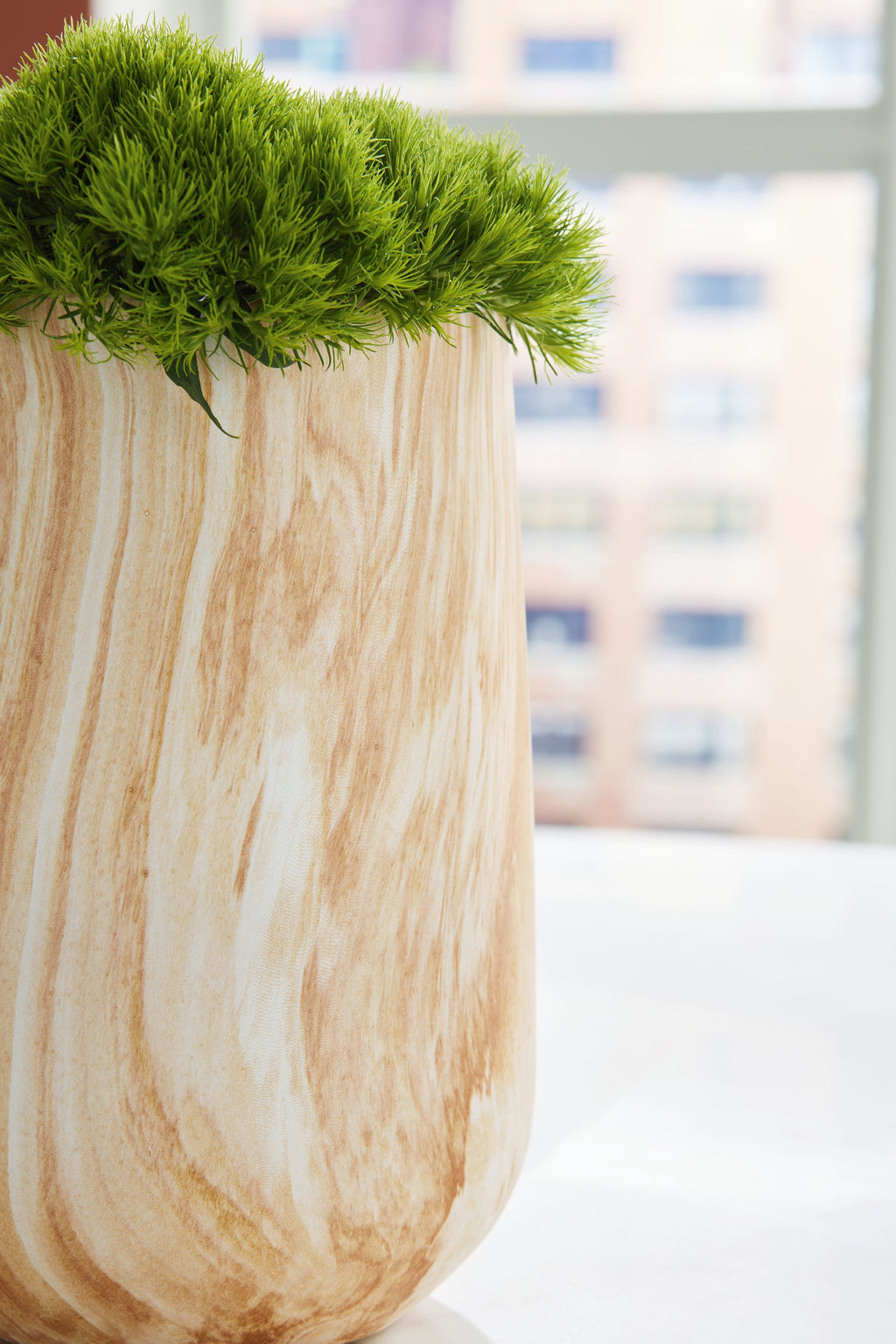 Beige marbled vase holding green grass, flared top and rounded base