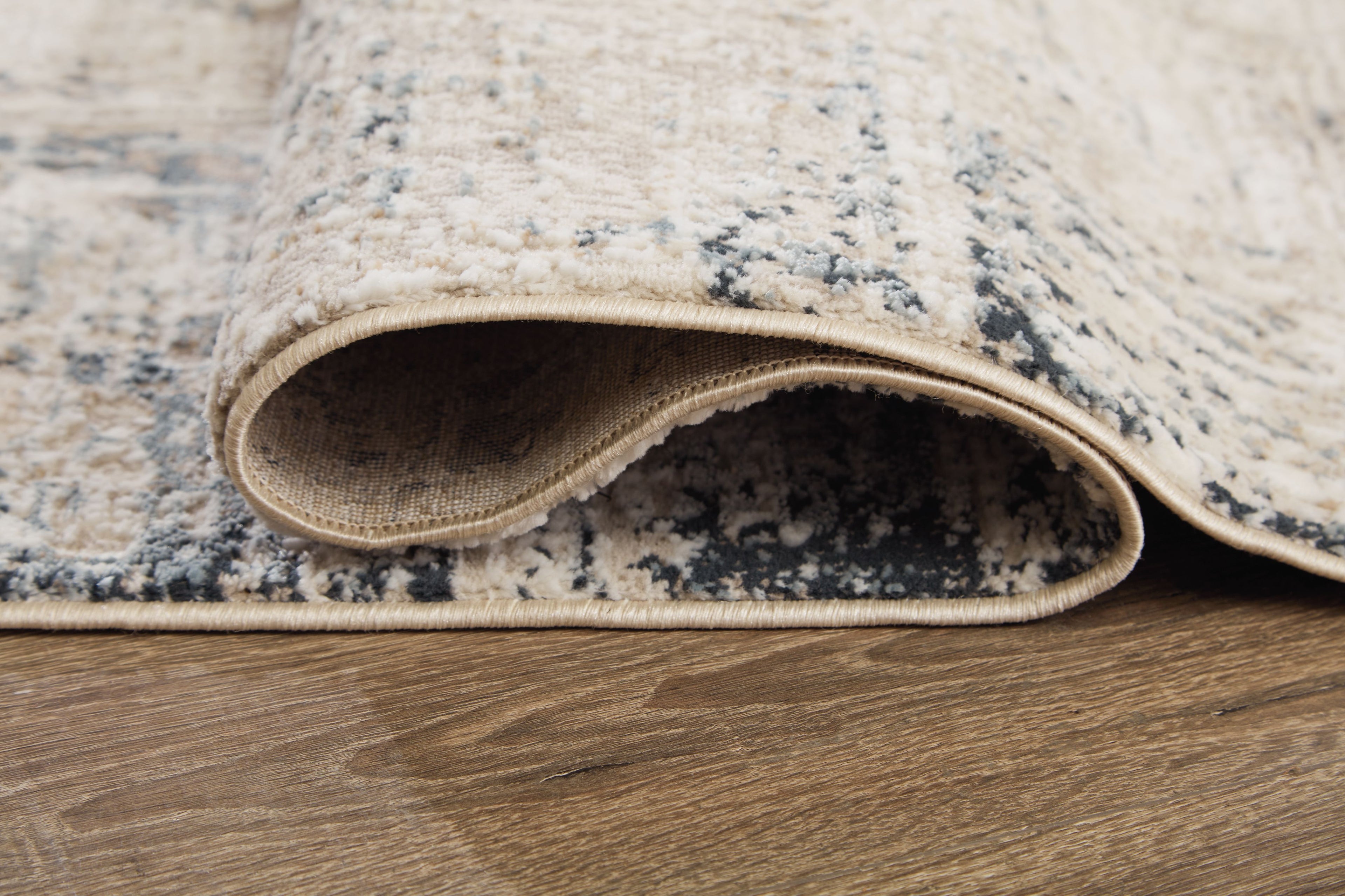 Cream area rug with blue-gray distressed pattern; rolled edge shows low profile.