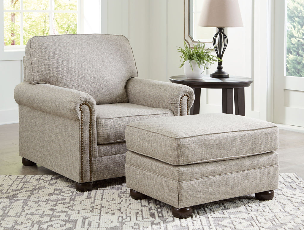 Light gray upholstered chair with matching ottoman and decorative trim on arms.