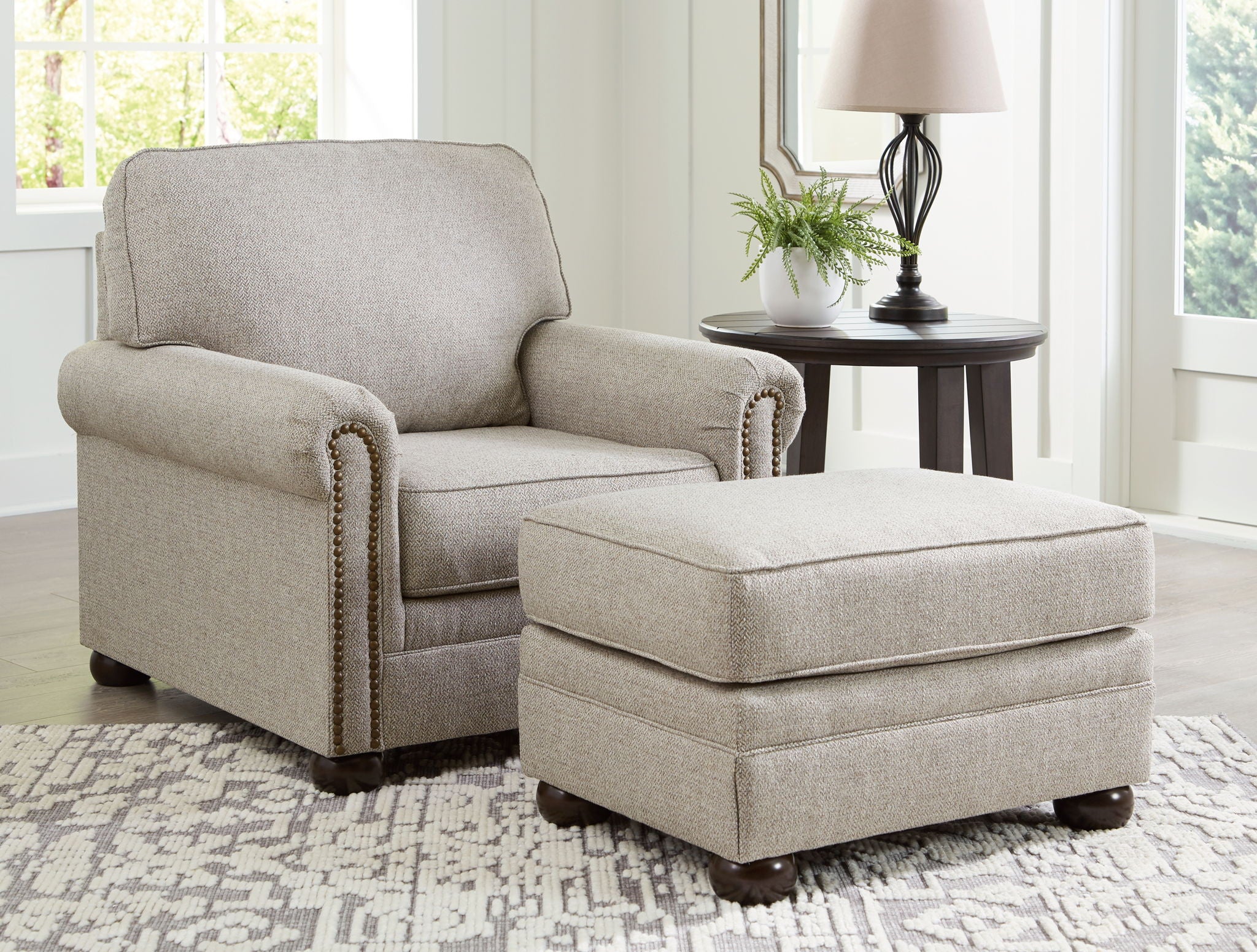 Light gray upholstered chair with matching ottoman and decorative trim on arms.