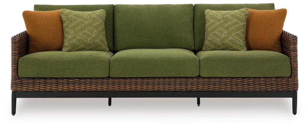 Green sofa with woven wicker frame, brown side pillows, and patterned cushions