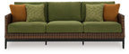 Green sofa with woven wicker frame, brown side pillows, and patterned cushions