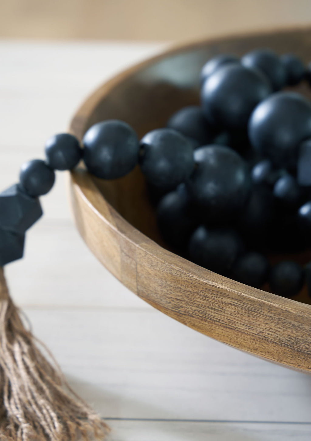 Natural brown wooden bowl filled with dark bead clusters and braided cord