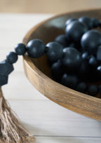 Natural brown wooden bowl filled with dark bead clusters and braided cord