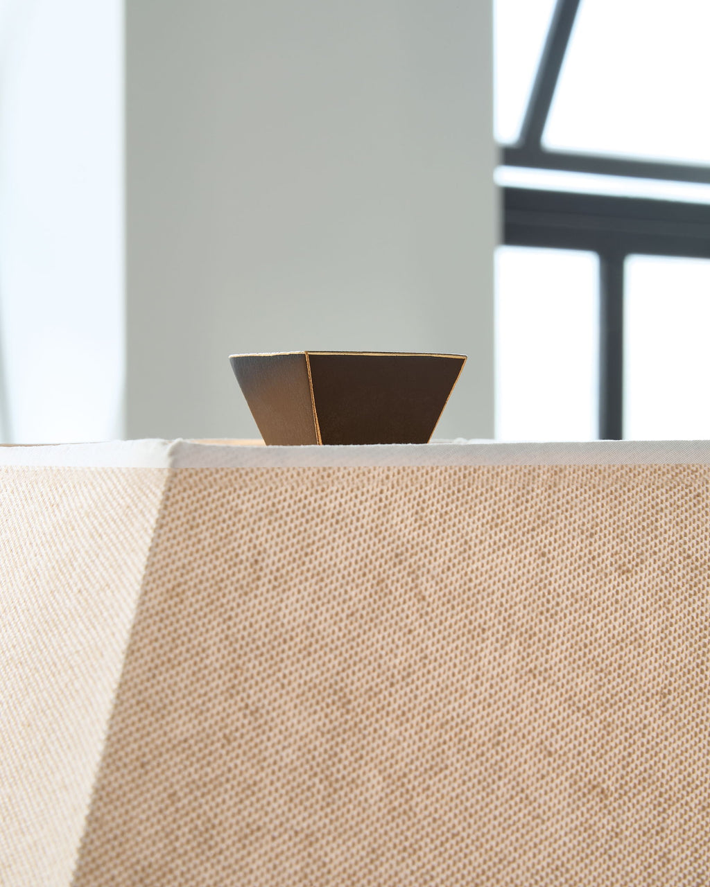Tan fabric lamp shade with brown interior and dark metal frame on a tabletop