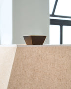 Tan fabric lamp shade with brown interior and dark metal frame on a tabletop
