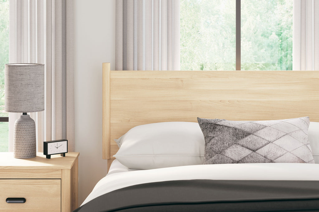 Light tan wood full-panel headboard behind bed pillow and quilt