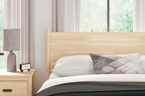 Light tan wood full-panel headboard behind bed pillow and quilt