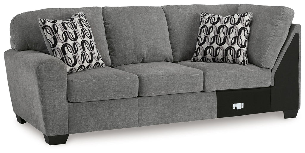 Gray sofa with corner wedge, two patterned throw pillows, and dark base panels