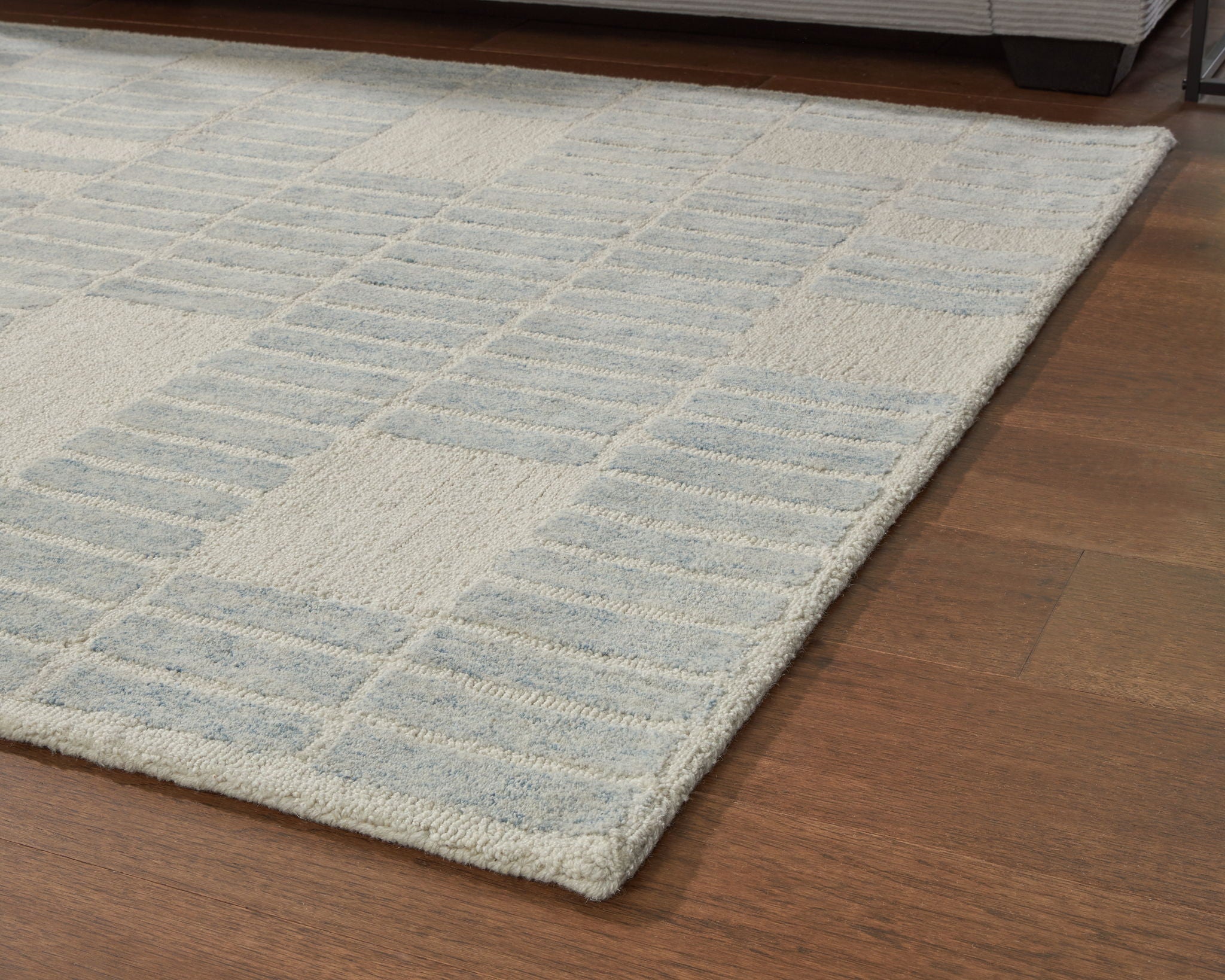 Light blue area rug with repeating grid pattern, folded edge on floor