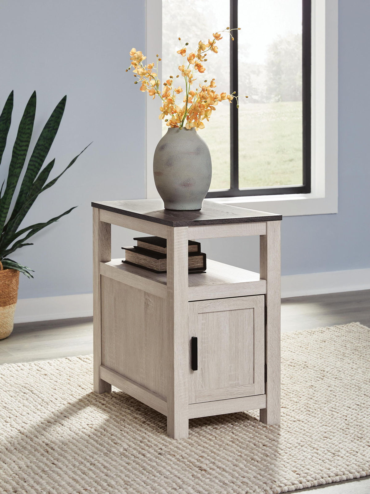 Chair side end table in light brown wood with open shelf and cabinet door with black pull