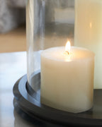 Glass cylinder candle holder with dark base, holding a lit white candle