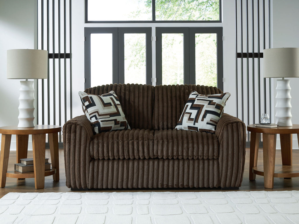 Dark brown corduroy loveseat with two geometric throw pillows, thick arms and back