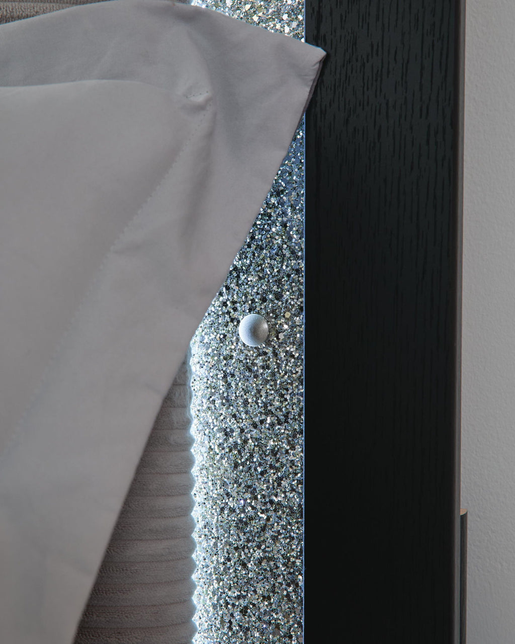 Upholstered headboard edge with glittery inset, silver button, and dark wood trim.