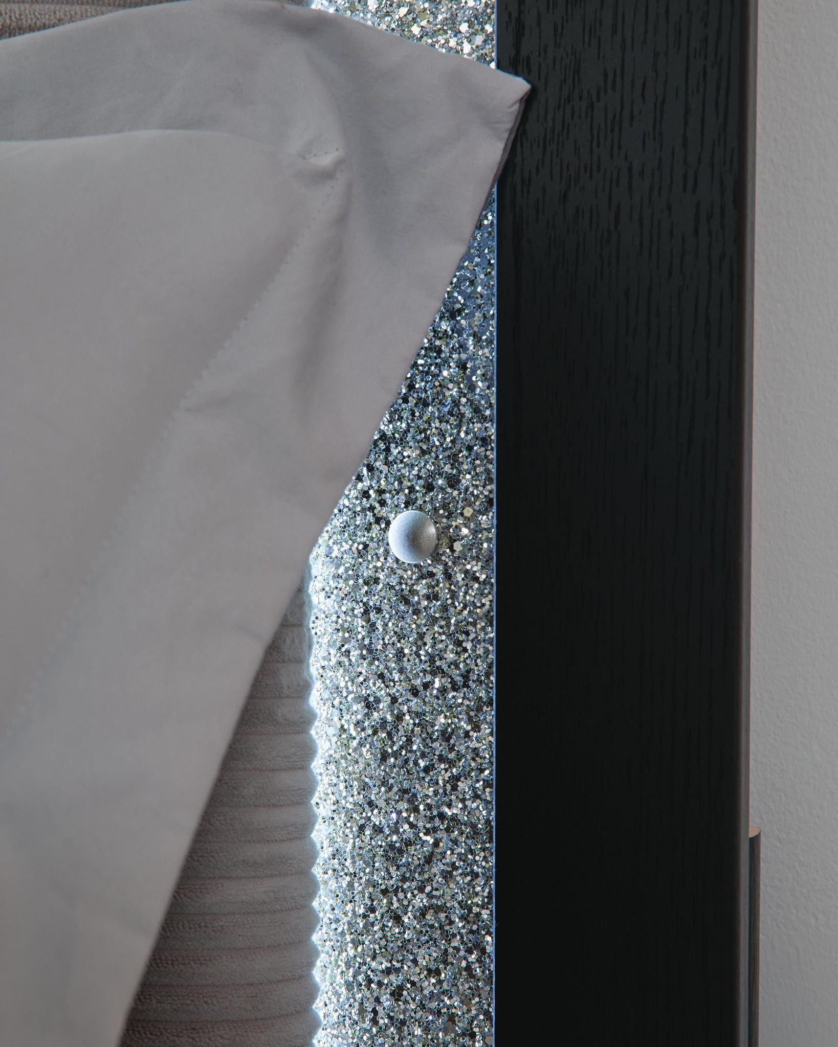 Upholstered headboard edge with glittery inset, silver button, and dark wood trim.