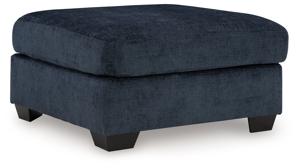 Navy upholstered ottoman with round-corner lid and dark block legs.