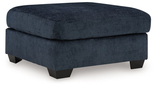 Navy upholstered ottoman with round-corner lid and dark block legs.