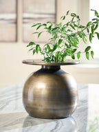 Bronze metal vase centerpiece with wide mouth on round stand, holding green stems and leaves.