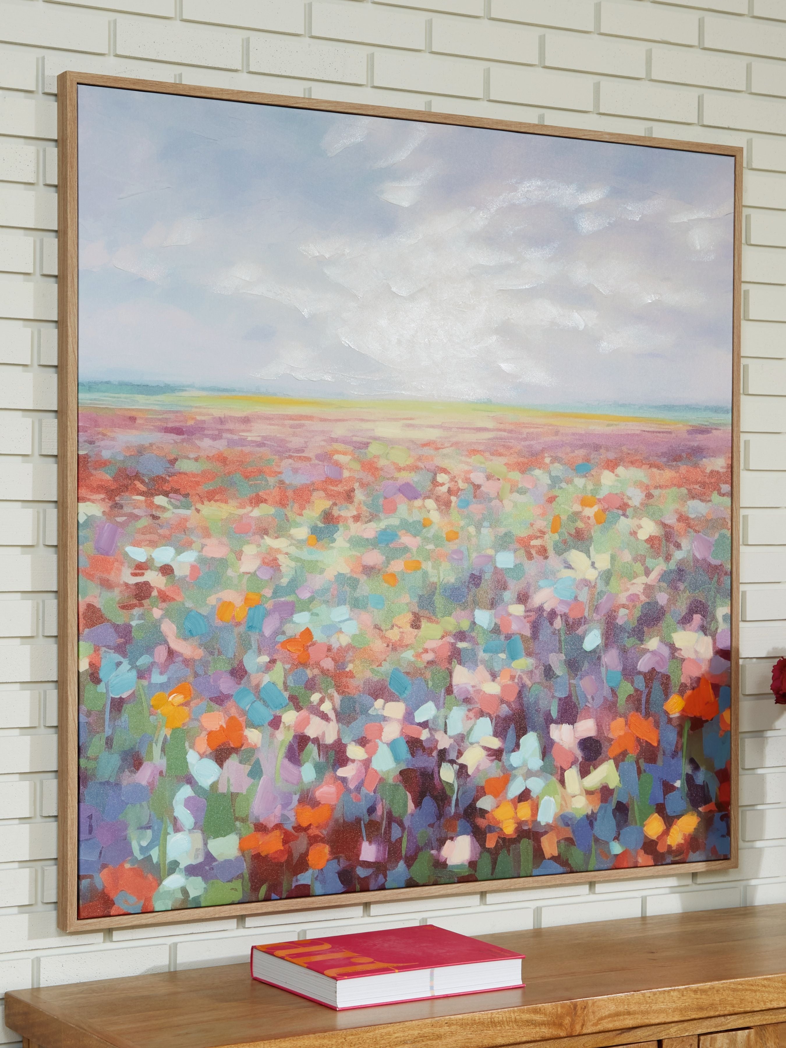 Abstract multicolor landscape wall art with wood-tone frame, mounted on white brick