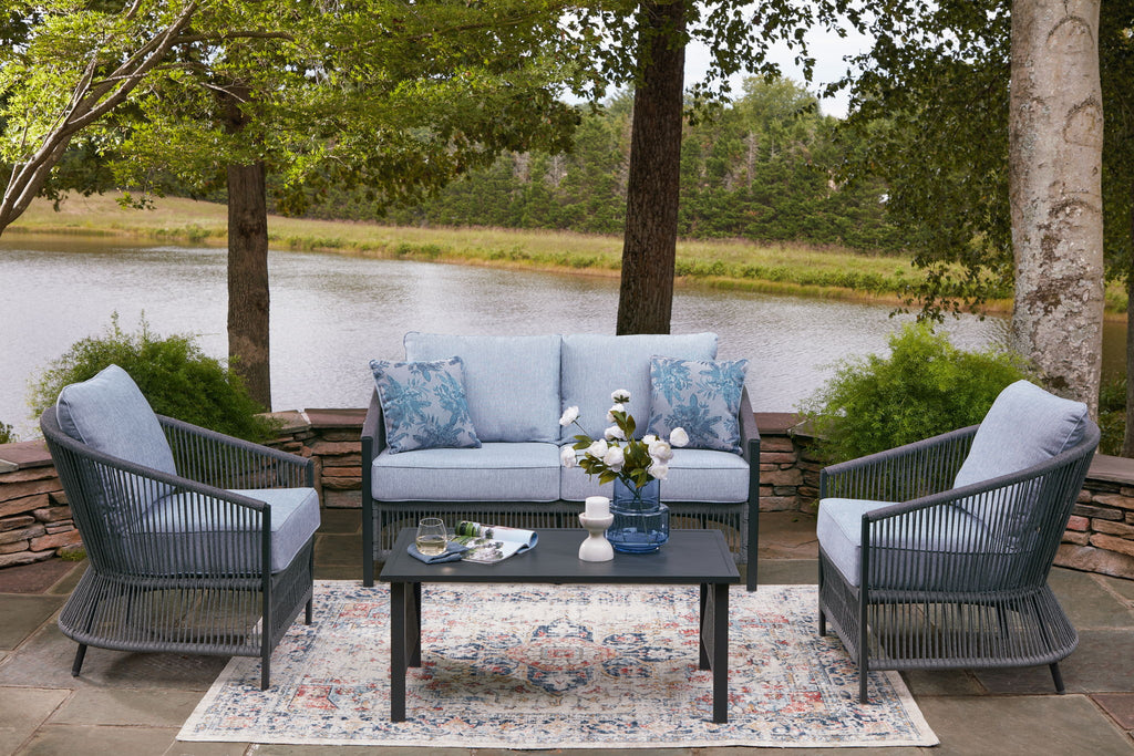 Outdoor loveseat and two armchairs with light gray cushions, blue pillows, and coffee table