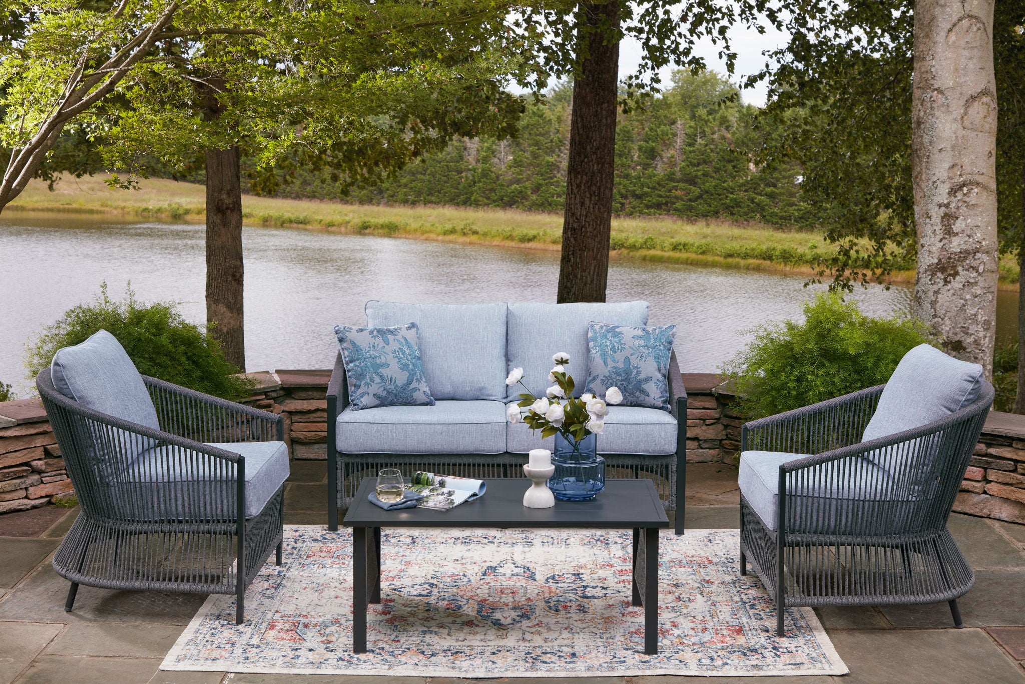 Outdoor loveseat and two armchairs with light gray cushions, blue pillows, and coffee table