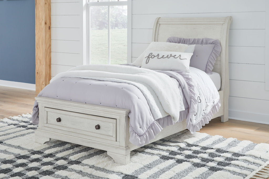 White sleigh bed with storage drawers and paneled headboard, styled with bedding.
