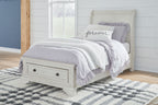 White sleigh bed with storage drawers and paneled headboard, styled with bedding.