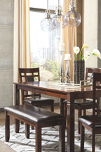 Brown dining table set with glass tabletop, four chairs, and dark cushioned bench