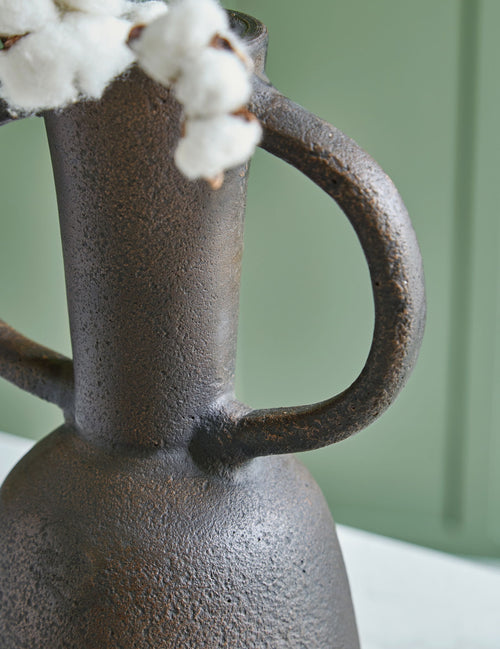 Distressed brown vase with loop handle, topped with white cotton stems.