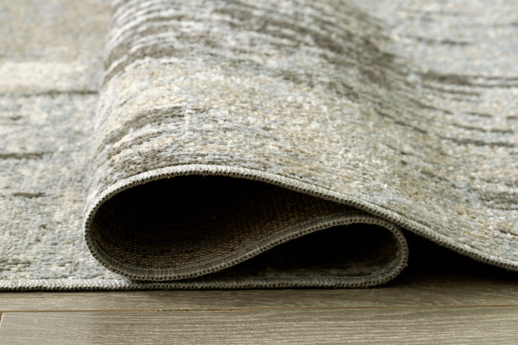 Rolled edge of washable area rug in beige and gray abstract texture, bound border