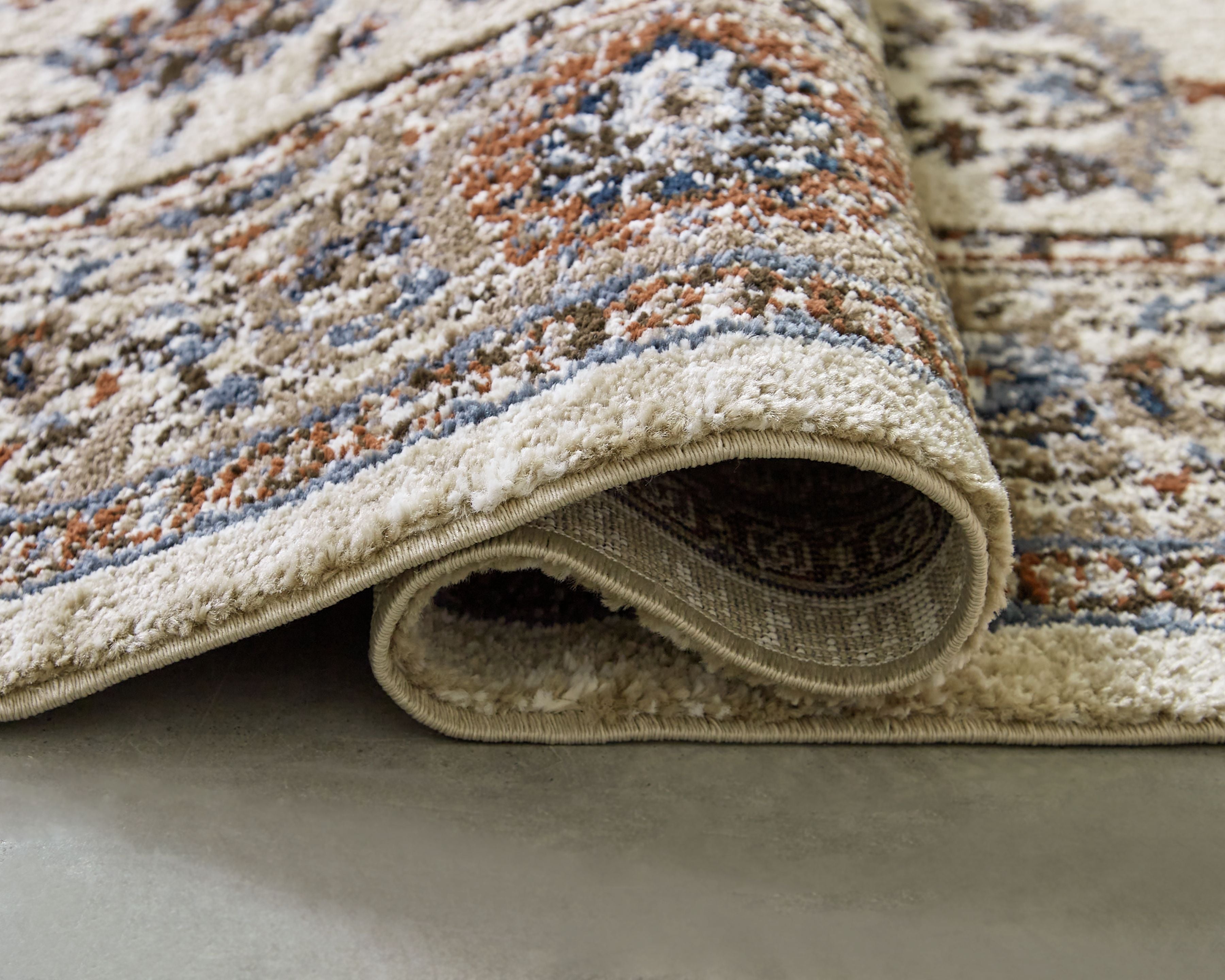 Beritham rug corner with textured pile and decorative pattern, cream edge binding visible