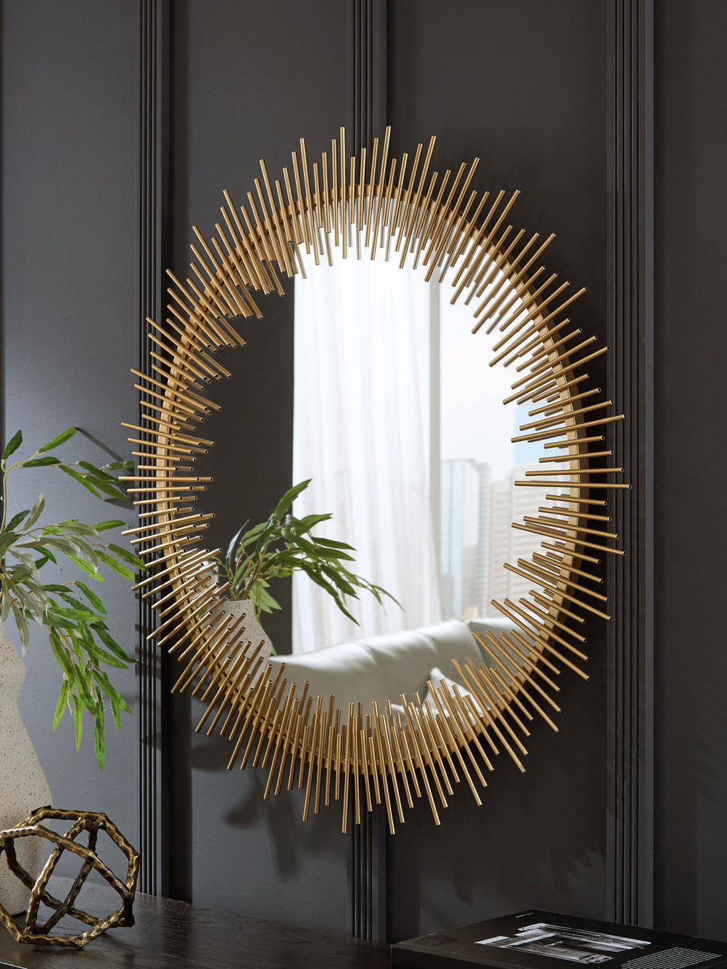 Gold circular accent mirror with radiating rods, reflecting window light