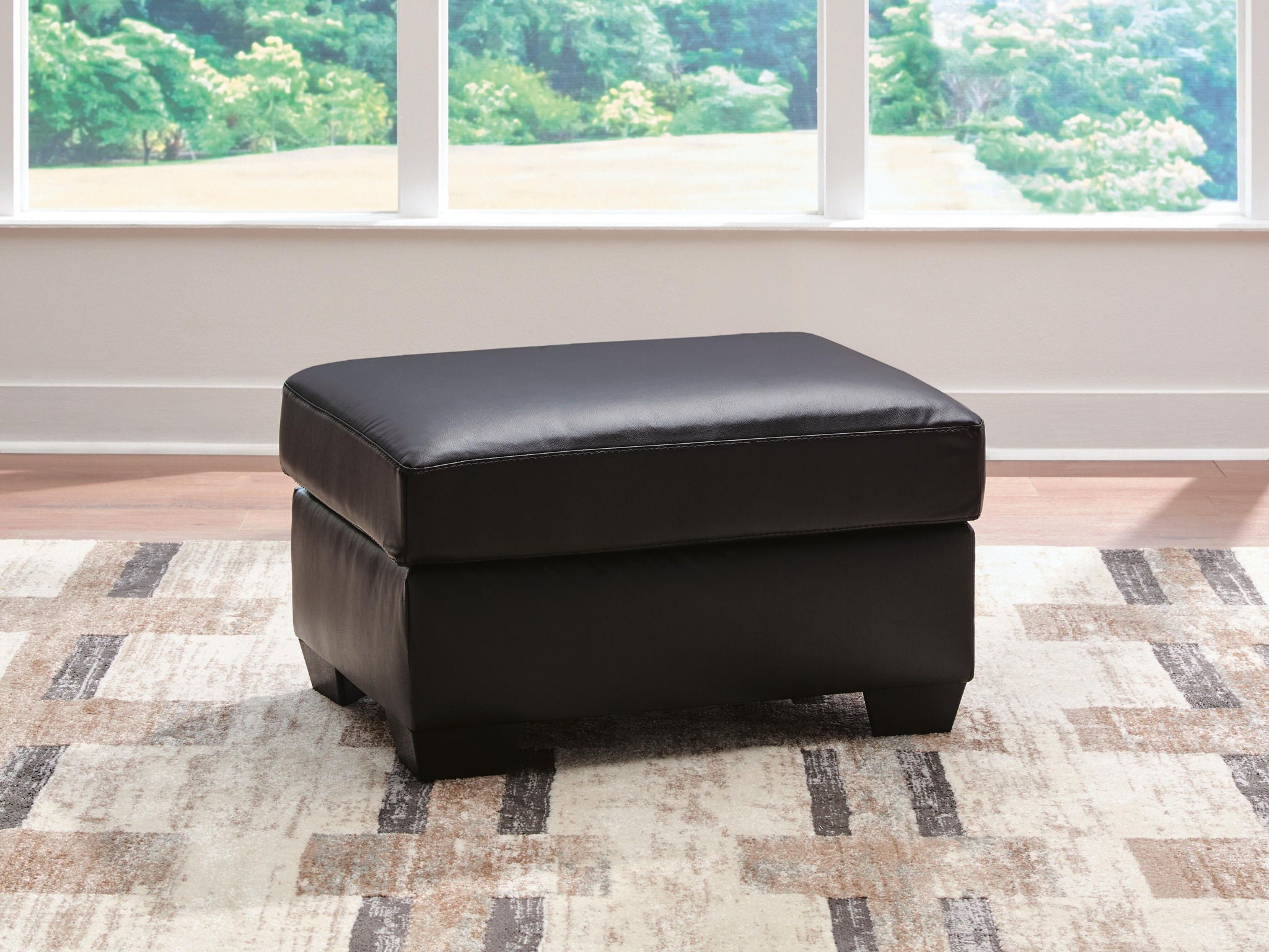 Glennbre ottoman in dark upholstery, padded top, rounded corners, short legs