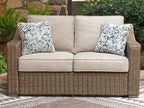 Outdoor loveseat with beige seat cushions, brown wicker frame, two patterned throw pillows